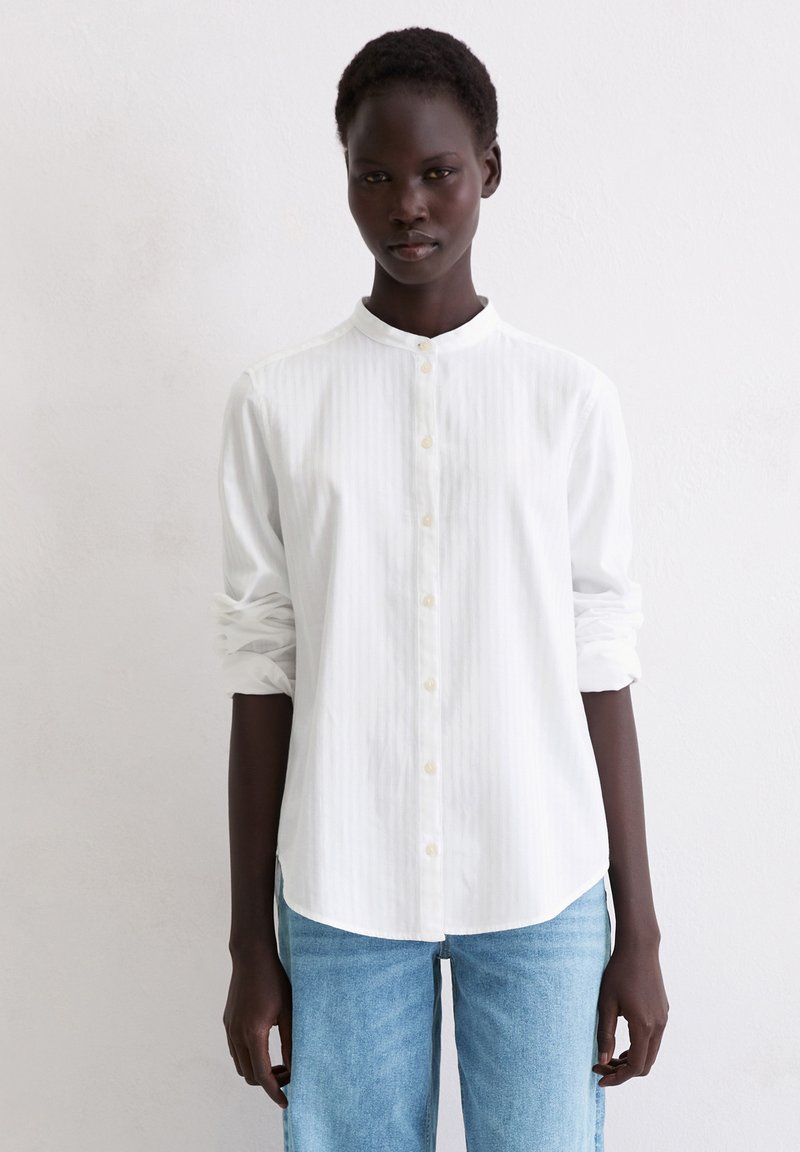 Biała koszula z kołnierzykiem zapinana na guziki, z pionowymi paskami, długie rękawy podwinięte na mankietach, zestawiona z jasnoniebieskimi jeansami. Prosty design, klasyczne dopasowanie.