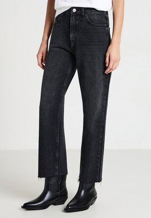 Jeans in denim nero con taglio dritto, caratterizzati da orli sfilacciati. Indossati con stivali alla caviglia neri con punta. Design semplice e pulito.