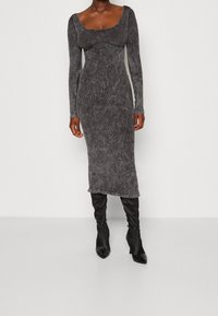 Szara midi sukienka z długim rękawem, dekoltem w serek i prążkowanym materiałem, w zestawieniu z dopasowanymi czarnymi kozakami za kolano z szpiczastymi носkami.