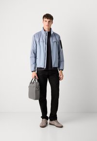 Pale blue jacket with a high collar and black accent, paired with a black shirt and pants. Holding a gray bag, wearing light sneakers.