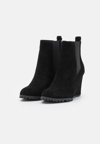 Bottes chelsea à talon compensé en suède noir avec des panneaux élastiques sur les côtés, bout rond et semelle en caoutchouc texturé pour une meilleure adhérence. Silhouette simple et épurée.