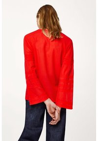 Rød linned-top med flagrende ærmer, der har horisontale striber. Bagudvisningen viser en simpel halsudskæring og en afslappet pasform. Kombineret med mørk denim.