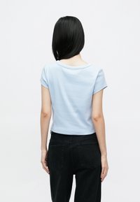 Light blue short-sleeve top with a round neckline, made from smooth fabric. Paired with black high-waisted jeans.
