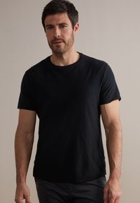 Svart t-shirt med rund hals och korta ärmar, tillverkad av mjukt tyg. Har en avslappnad passform och en något rundad nederkant. Enkel och mångsidig design.