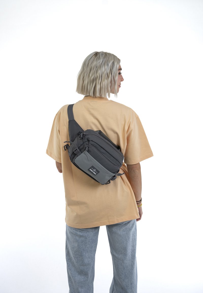 Borsa a tracolla grigia con più scomparti e tracolla regolabile, realizzata in tessuto resistente; presenta una tasca anteriore più piccola e cerniere.