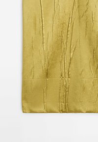 Tissu en satin doré avec une texture froissée et une couture horizontale près du bord inférieur sur un fond blanc.