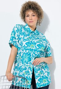 Camicia corta manica in tessuto turchese con colletto. Presenta un audace motivo floreale e chiusura a bottoni, abbinata a jeans blu scuro.