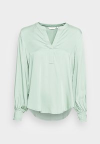 Blusa verde chiaro a maniche lunghe con scollatura a V, polsini plissettati e orlo asimmetrico. Realizzata in un tessuto morbido e fluido.