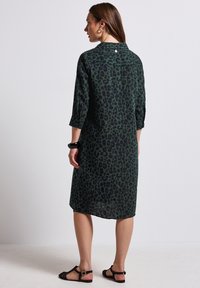 Abito verde con stampa leopardata, maniche a tre quarti, una chiusura a bottoni sul retro e una vestibilità ampia che scende appena sopra le caviglie.