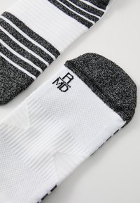 Meias atléticas listradas em preto e branco com textura canelada, apresentando um bico e um calcanhar sólidos em preto, e um logotipo da marca em costura preta.