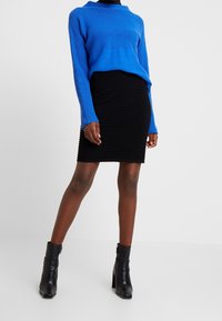 Modrý pletený svetr s kulatým výstřihem, kombinovaný s černou skládanou sukní. Model má na sobě černé kotníkové boty s masivním podpatkem.