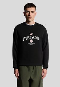 Felpa nera con scollo rotondo, con logo Lyle & Scott in bianco e rosa, abbinata a pantaloni cargo verde oliva.