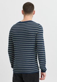 Camicia a maniche lunghe di colore blu navy con strisce orizzontali bianche e azzurre. Presenta un collo girocollo e polsini a costine con una texture morbida.