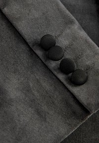 Tissu gris à texture douce, présentant trois boutons noirs côtelés et des détails de couture visibles le long du bord.