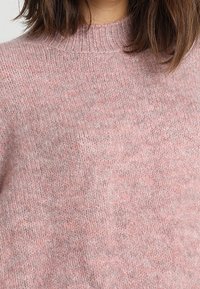Rosa gestrickter Pullover mit hohem Kragen, der eine weiche Textur und subtile Farbvariationen im gesamten Stoff aufweist.