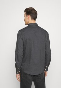 Camisa de manga larga gris oscuro con cuello abotonado y tres botones en cada puño, que presenta una textura de tela suave y un dobladillo curvado.