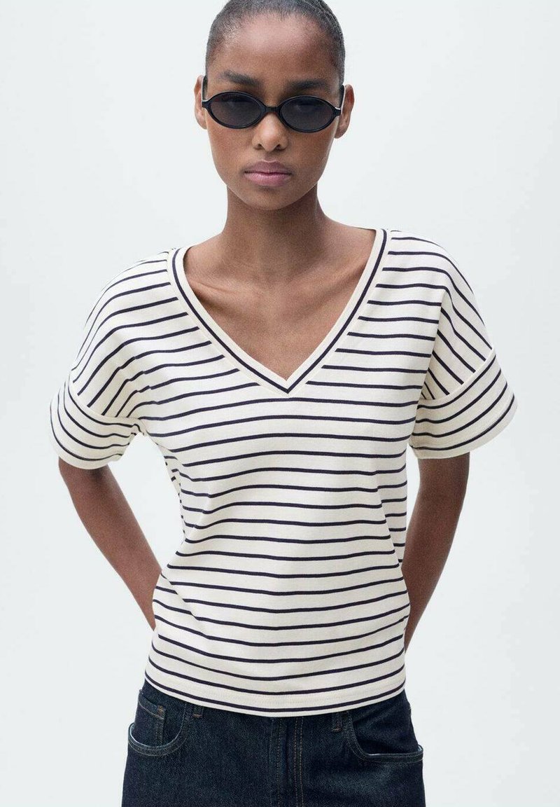 Randig, kortärmad V-ringad skjorta i krämfärg med marinblå ränder, tillverkad av mjukt tyg, i kombination med mörka jeans. Enkel, avslappnad design.