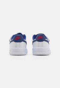 White sneaker with blue accents, textured overlays, and red branding. Features a padded collar and rubber outsole for grip.