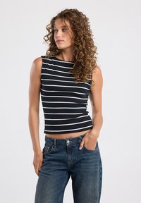 Black and white striped sleeveless top with a fitted design, soft texture, and a crew neckline, paired with blue high-waisted jeans.