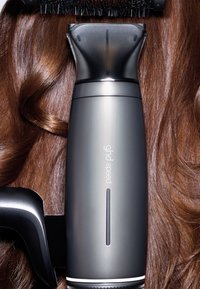 Sèche-cheveux ghd Speed gris reposant sur des cheveux bruns ondulés et brillants, mettant en valeur la finition mate et le design élégant de l'appareil.