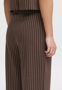 Pantalons rayés marron avec un crop top, présentant des rayures verticales blanches. Le tissu semble doux avec un léger éclat.