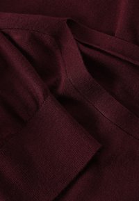 Burgunderfarbiger Strickstoff mit glatter Textur, ausgestattet mit einem umgeschlagenen Bündchen und sanften, gleichmäßigen Nähte. Das Design ist einfach und nahtlos.