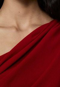 Roter, drapierter Stoff mit weicher Textur, der ein fließendes Design präsentiert und den Ausschnitt sowie den Schlüsselbeinbereich betont.