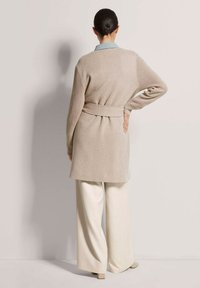 Beige gestrickte Cardigan mit einem Bindegürtel, kombiniert mit weiten cremefarbenen Hosen. Rippstruktur an den Ärmeln, durchgehend hellblauem Kragenakzent.