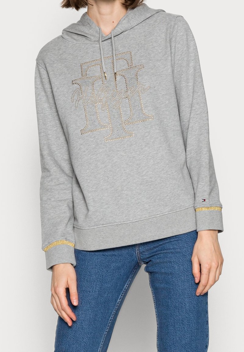 Grijze hoodie met een sprankelende logodesign, een kangoeroezak en gouden accenten op de manchetten. Zachte, текстууризованная stof.