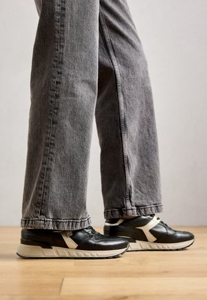 Zwarte en beige sneakers met een glad leren bovenwerk, gestructureerde accenten en een dikke zool. Draag ze met grijze, iets losse denim jeans.