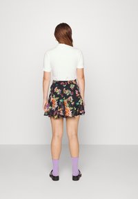 Black floral skirt with colorful patterns, paired with a plain white top. Worn with purple socks and black shoes, viewed from the back.