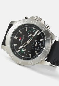 Edelstahl-Uhr mit schwarzem Zifferblatt, silbernen Akzenten und Chronographen-Funktionen. Schwarzes Gummiarmband. Deutliche Ziffern auf der Lünette.