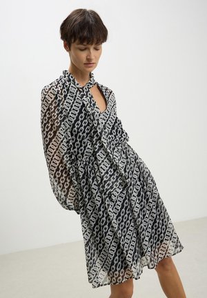 Abito a catena in bianco e nero, realizzato in tessuto trasparente, con scollatura a chiave e maniche voluminose, e gonna svasata.