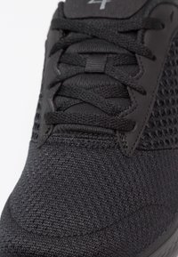 Zwarte sportieve schoen met een gebreide textuur, netpanelen, ronde veters en een gladde rubberen zool met subtiele branding op de tong.