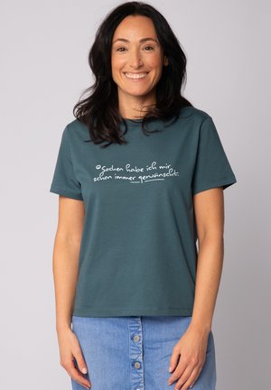 Tijgroene katoenen T-shirt met korte mouwen en een ronde hals, met daarop witte handgeschreven tekst aan de voorkant. Gecombineerd met een denim rok met knopen aan de voorkant.