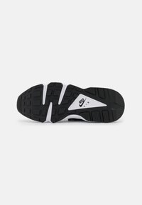 Semelle de chaussure de sport noir et blanc avec du caoutchouc texturé, présentant un motif distinct, des accents surélevés et le logo Nike Air.