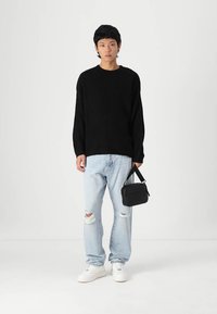 Un pull noir côtelé, un jean déchiré bleu clair, des baskets blanches, et un petit sac bandoulière noir. Look décontracté et ample avec des textures distinctes.