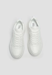 Bílé tenisky s hladkým koženým povrchem, s šněrováním, polstrovaným jazykem a texturovanou podrážkou. Žádné viditelné vzory.