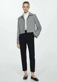 Chaqueta gris corta con cuello, dos botones frontales y mangas largas, combinada con pantalones negros ajustados y zapatos planos negros.