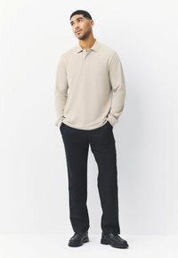 Beige pitkähihaisen polopaidan, jossa on kaulus, yhdistetty mustiin housuihin ja mustiin kenkiin; sileä kangas, istuva malli, vähäeleinen koristelu.