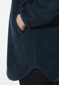 Marine fleece jack met een gestructureerde afwerking, afgeronde onderkant en zijzak. De randen zijn afgewerkt in een donkerdere tint die het ontwerp accentueert.