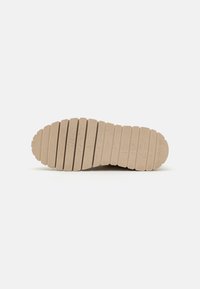 Suela de goma beige con ranuras horizontales y una superficie texturizada. Se pueden ver un tacón redondeado y patrones de tracción definidos.