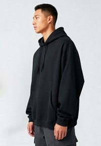 Felpa con cappuccio nera realizzata in tessuto morbido, con tasca a marsupio davanti, polsini e orlo rigati. Vestibilità rilassata e design minimal.