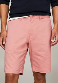 Pantalones cortos rosa claro hechos de una mezcla de algodón, con cierre de botón, trabillas para cinturón y una textura limpia y suave. Largo a medio muslo.