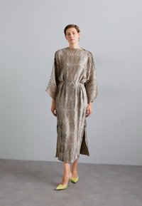 Light brown, textured dress with a loose fit, kimono sleeves, and a waist tie; features a side slit. Paired with yellow high-heeled shoes.