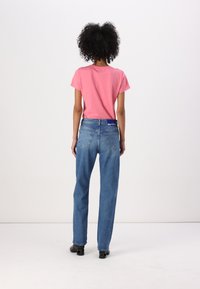Pink t-shirt and blue denim jeans worn together. Jeans are relaxed fit, featuring two back pockets and a blue waistband label. Smooth texture.