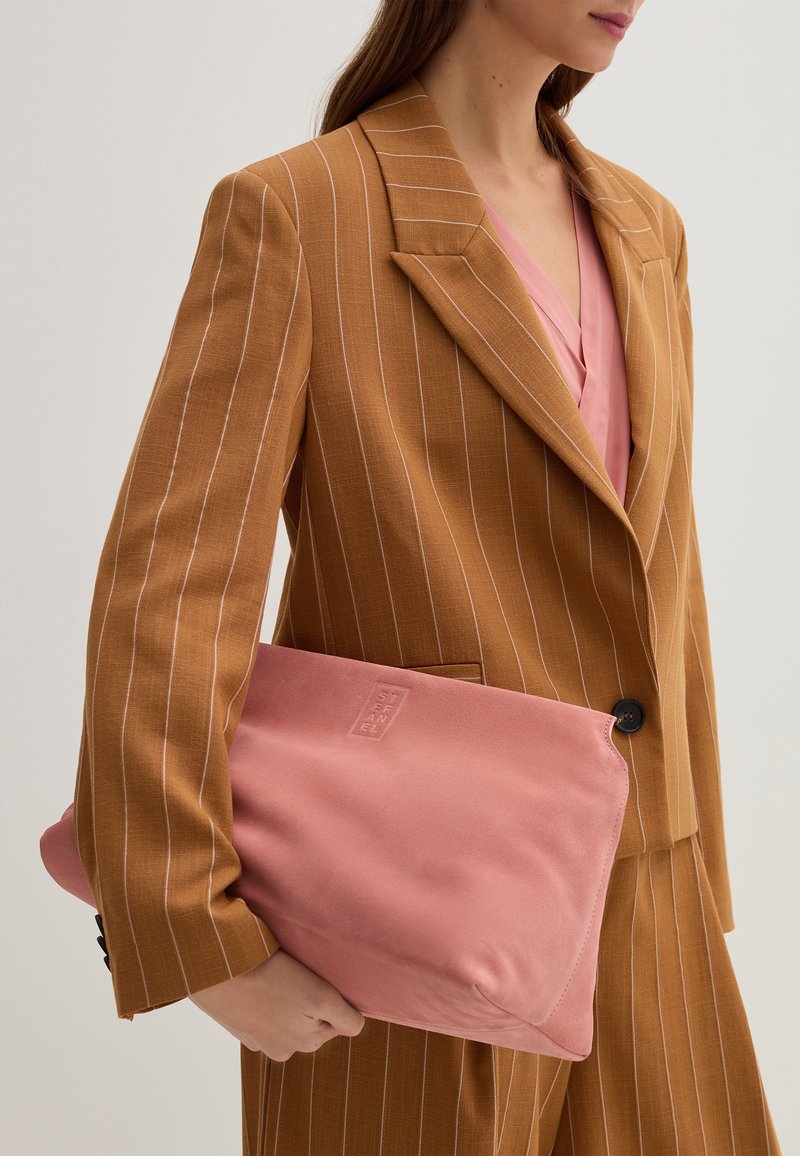 Blazer marrone a righe sottili su una maglia rosa, con una clutch bag rosa chiaro dalla superficie texture e con dettaglio logo.