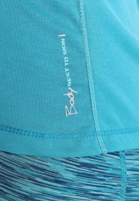 Tyrkysový sportovní top vyrobený z prodyšného materiálu. Disponuje jemně růžově potištěným logem a strukturovaným prošíváním podél lemu.