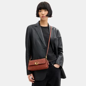 Jeune personne aux cheveux noirs courts, portant un blazer et un pantalon en cuir noir, portant un sac bandoulière en daim marron avec boucle dorée.