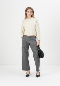 Maglione beige a maglia con design cropped, abbinato a pantaloni cargo grigi a gamba larga con tasche laterali e décolleté neri a punta.
